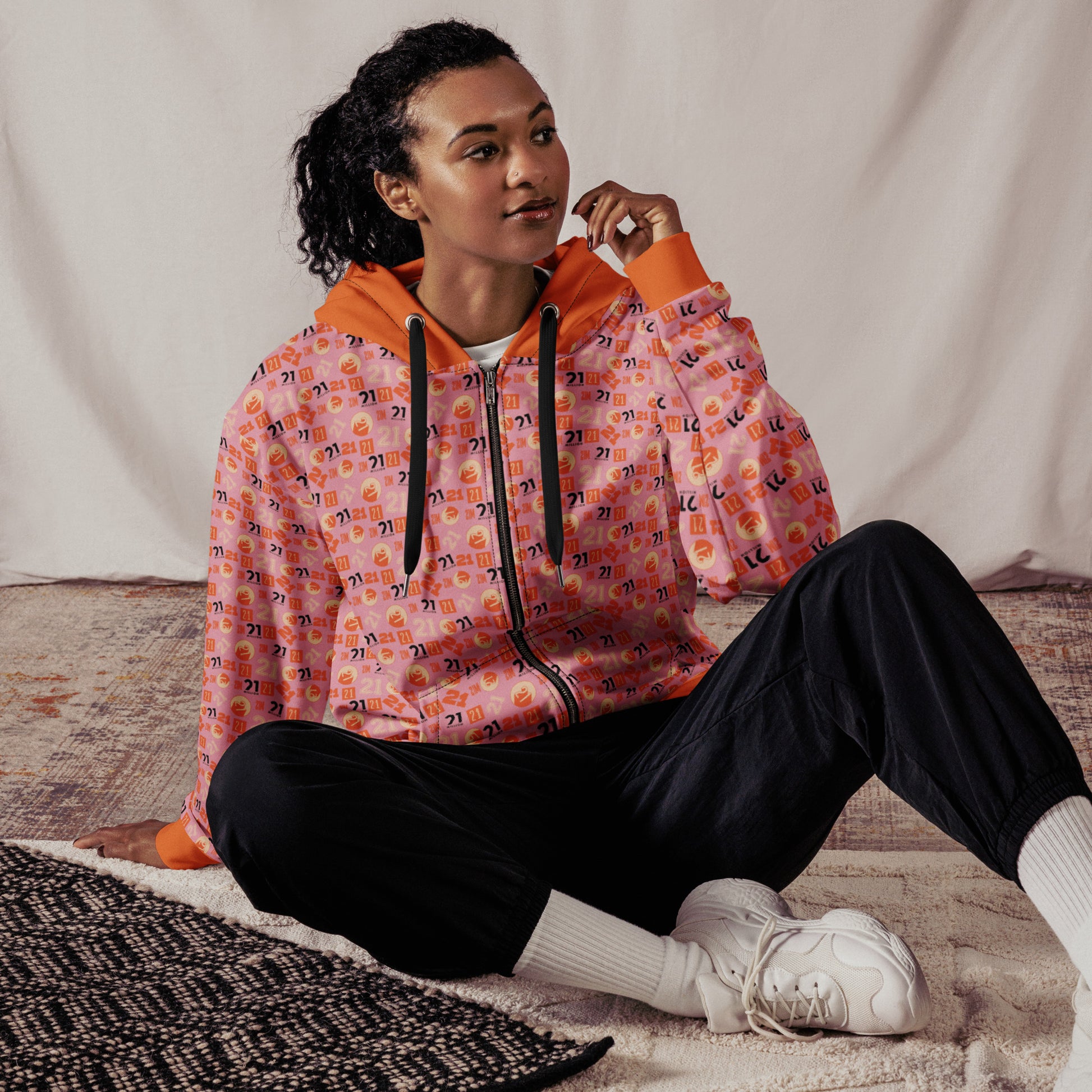 Person wearing an pink and orange 21 patterned hoodie sitting on a textured surface.